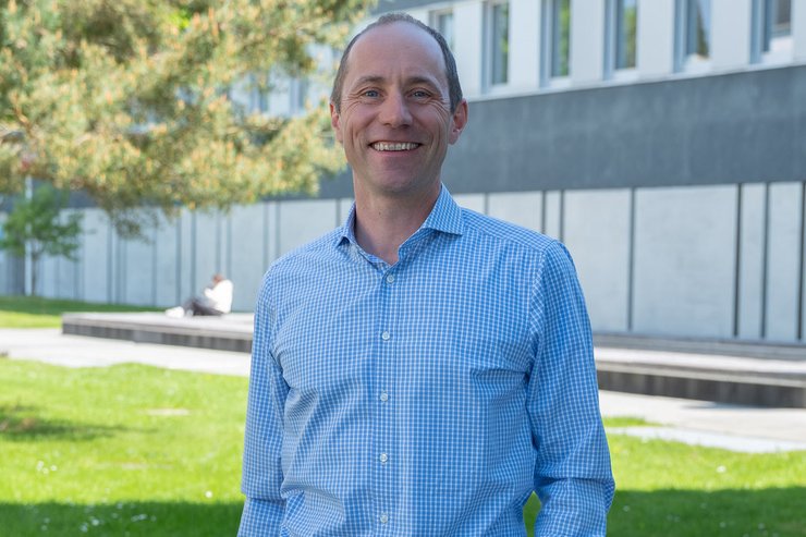 Professor der Hochschule Kempten steht auf dem Campus vor einem Hochschulgebäude.