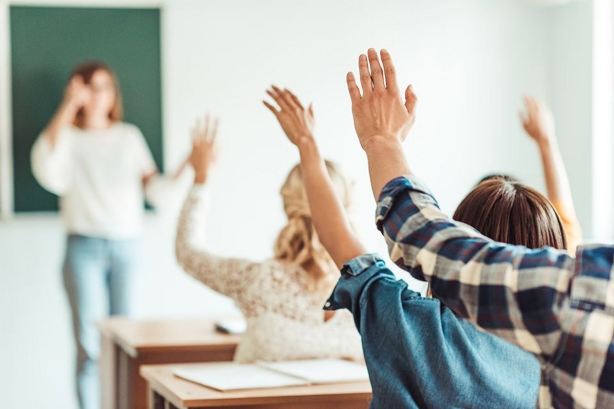 Bibliothekskurse für Schulen In einem Klassenraum melden sich Schüler, während ein Lehrer vor einer Tafel steht