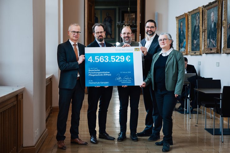 Dr. Rainer Hutka, Amtschef im Bayerischen Staatsministerium für Gesundheit, Pflege und Prävention sowie vom Bayerischen Zentrum Pflege Digital Prof. Dr. Mario Jokisch, Alexander Karl, Dr. Florian Fischer und Dr. Jana Brix halten den Förderscheck über rund 4,5 Millionen Euro in den Händen.